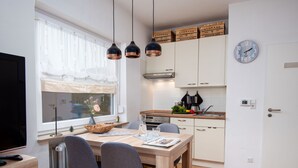Una cocina moderna con armarios blancos, una mesa de comedor de madera y un ventanal con cortinas de gasa.