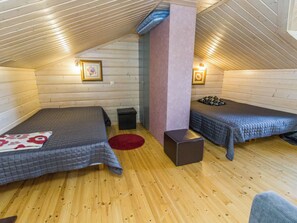 A cozy attic bedroom with two beds, a red rug, and wooden walls.