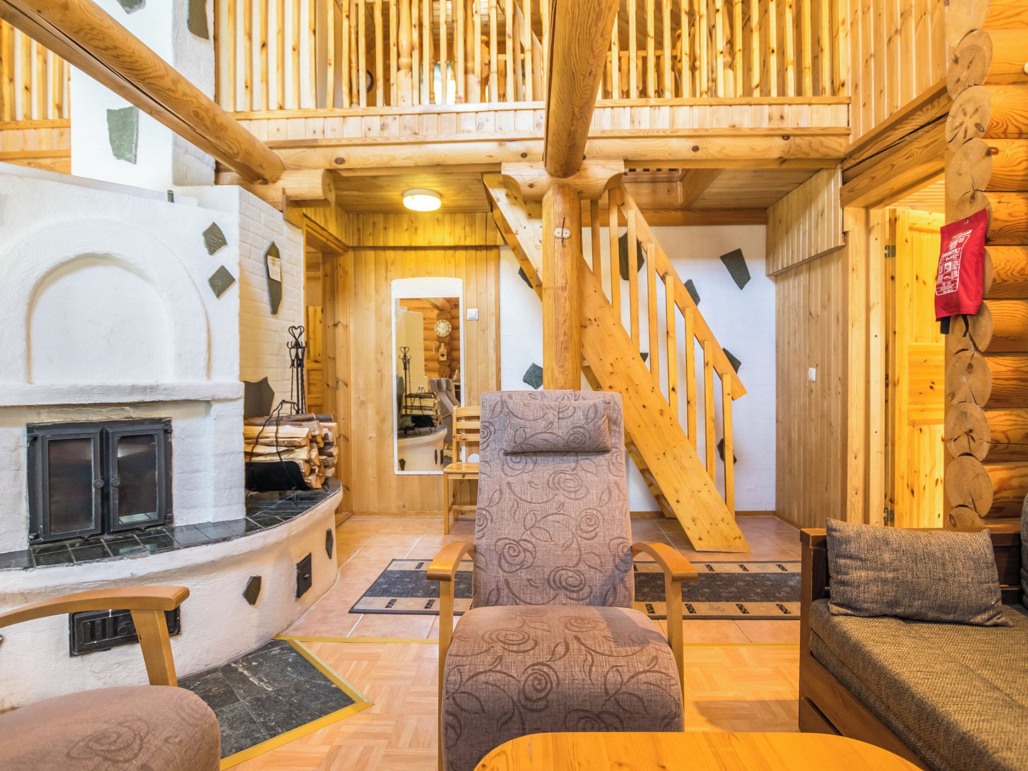 A log cabin interior with a fireplace, wooden staircase, and a cozy seating area.