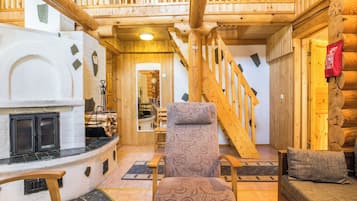 A log cabin interior with a fireplace, wooden staircase, and a cozy seating area.
