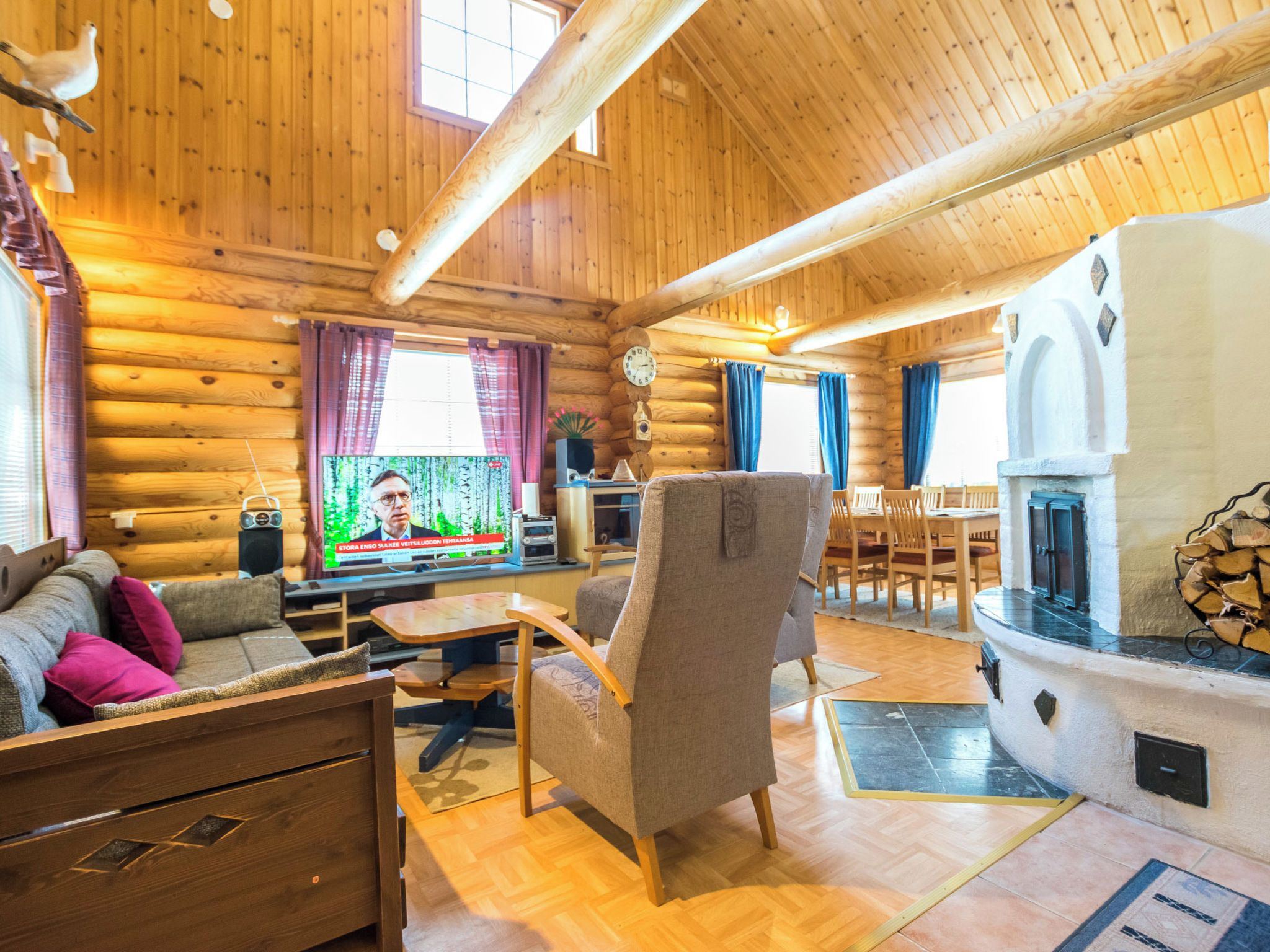 A log cabin interior with a wooden ceiling, a television, a fireplace, and a dining area.