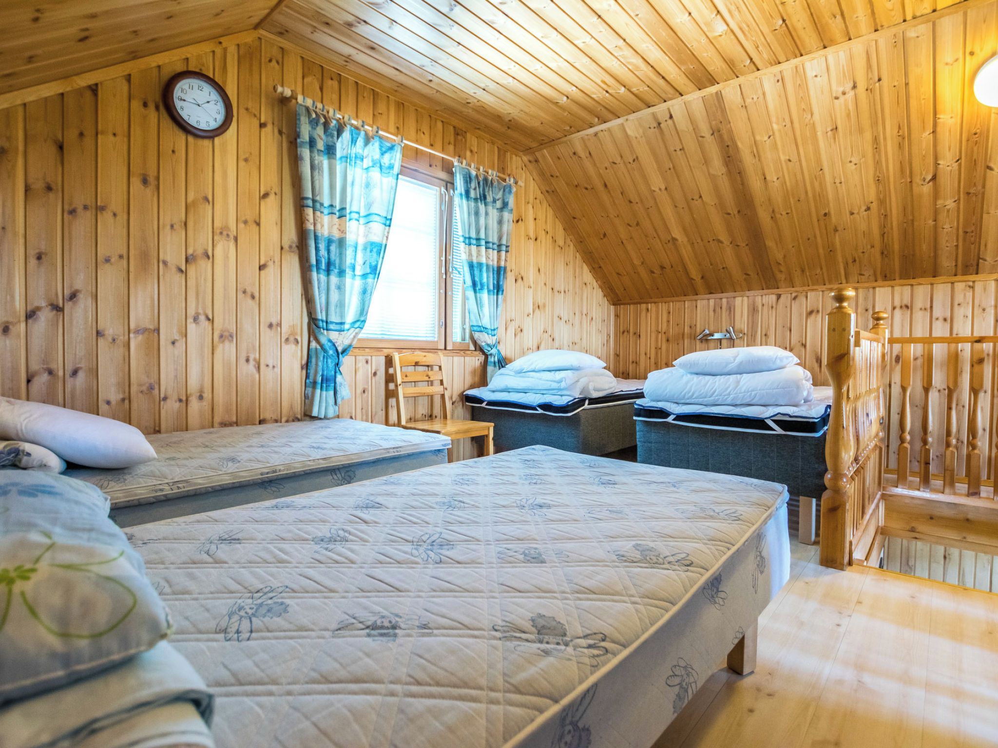 A cozy wooden cabin room with two beds, a wooden ceiling, and a clock on the wall.