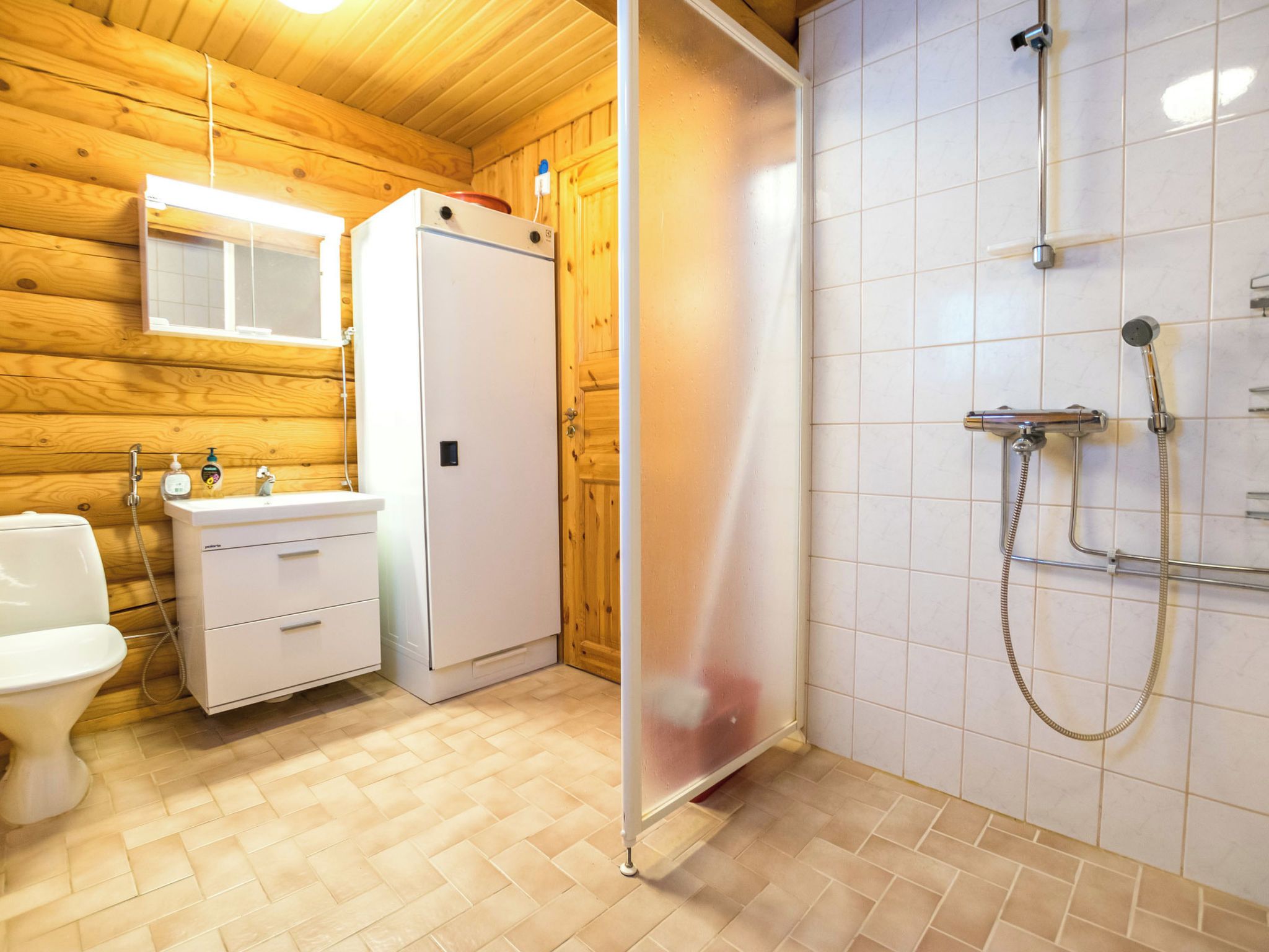 A bathroom with a wooden interior, a white sink, a toilet, and a shower area.