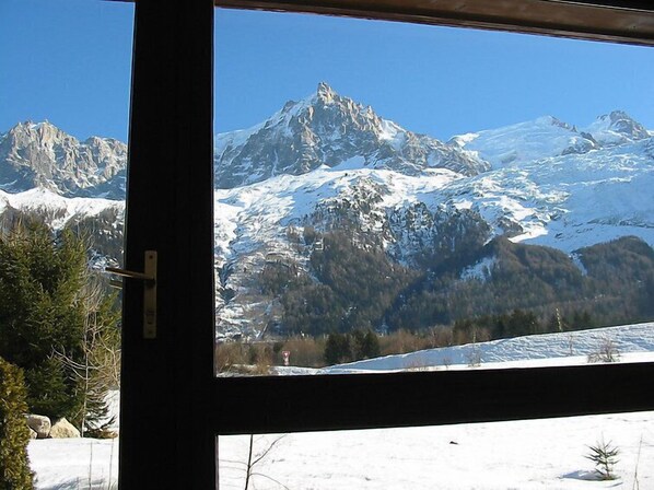 A mountain view through a window, featuring snow-covered peaks and a forested valley.