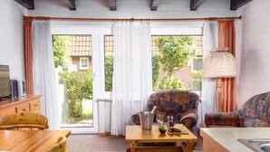 Een gezellige woonkamer met een houten tafel, twee stoelen, een gestreept sofa en uitzicht op een tuin door grote ramen.