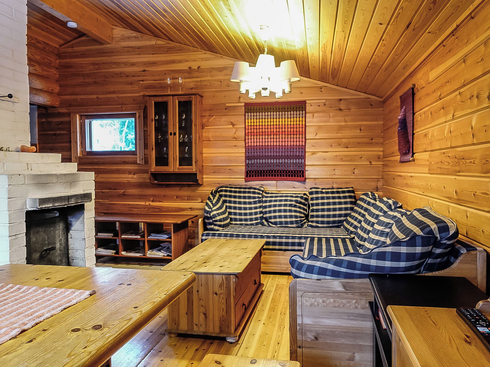 Ein gemütliches Blockhaus-Interieur mit Holzbalkendecke, einer Couch, einem Fernseher und einem Kamin.