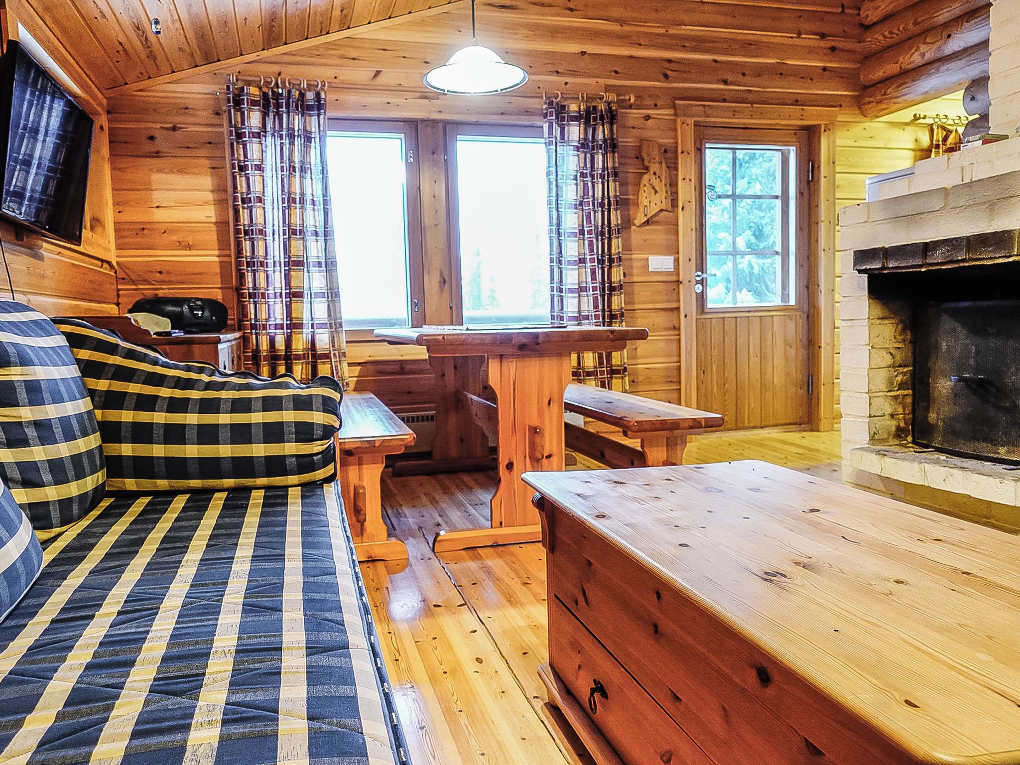 A cozy cabin interior with a sofa, a wooden bench, a fireplace, and plaid curtains.