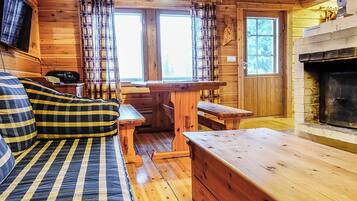 A cozy cabin interior with a sofa, a wooden bench, a fireplace, and plaid curtains.