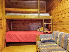 Una cama litera con escalera, una colcha roja y un sofá estampado con almohadas.