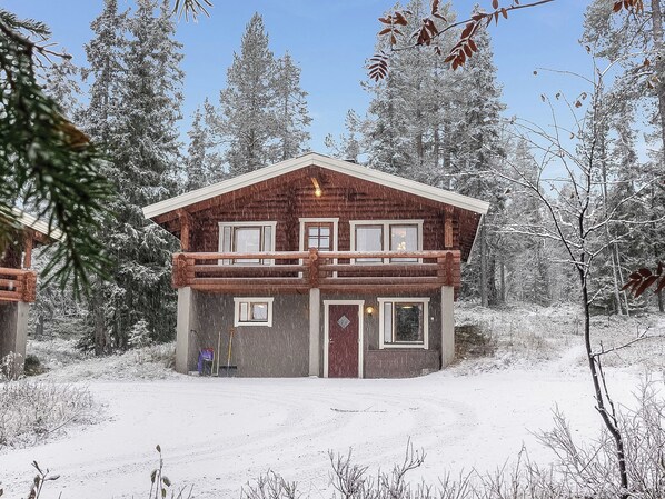 A two-story log cabin with a balcony, surrounded by snow-covered trees. - Oloskammi 5 by Interhome (Muonio)