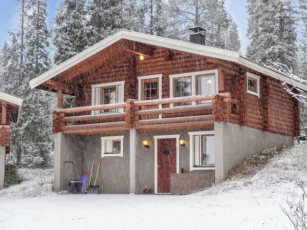 Una cabaña de troncos de dos pisos con un balcón, rodeada de árboles nevados.