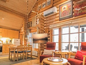 A log cabin interior with a dining area, a TV mounted on the wall, and a large window.