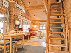A log cabin interior with a dining area, a red armchair, a sofa, and a wooden ladder.