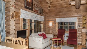 Ein gemütliches Blockhaus-Interieur mit einem Holzespeise Tisch, einer Couch, einem roten Sessel und einem Fernseher.