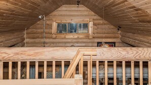 Ein Schlafzimmer im Dachgeschoss mit Holzwänden, einem Fenster, einer Deckenleuchte und einer Holztreppe.