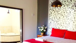 A bedroom with a bed, a small table with a vase of flowers, a red pillow, and a wall with floral wallpaper. - Pousada Grande Rio (Pirapora)