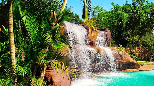 A waterfall cascading into a turquoise pool surrounded by lush greenery and rocks. - Pousada Grande Rio (Pirapora)