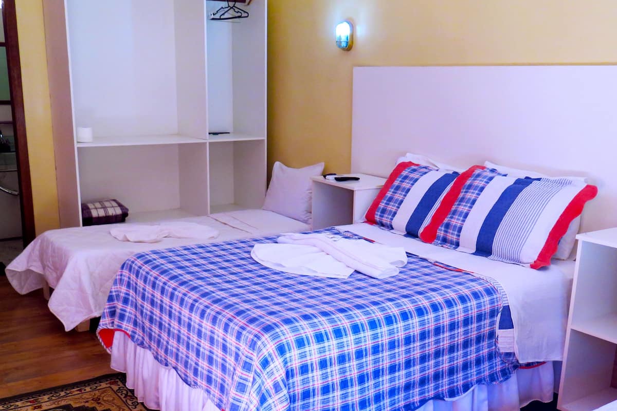 Una habitación de hotel con dos camas, un armario, una mesita de noche y una alfombra estampada.