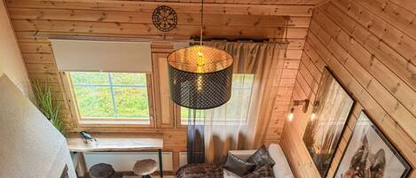 L’intérieur d’un chalet accueillant, avec un canapé, une table basse ronde en bois, un bureau et une grande fenêtre.