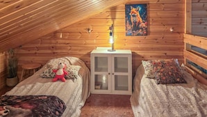 Un dormitorio acogedor en un ático con paredes de madera, techo inclinado, dos camas con ropa de cama floral, una mesita de noche con una lámpara y un cuadro de un zorro.