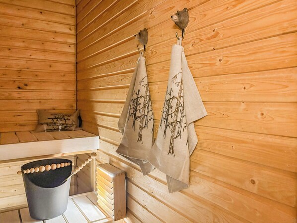 L’intérieur d’un chalet en bois, avec un sauna, des serviettes suspendues à des crochets et un seau.
