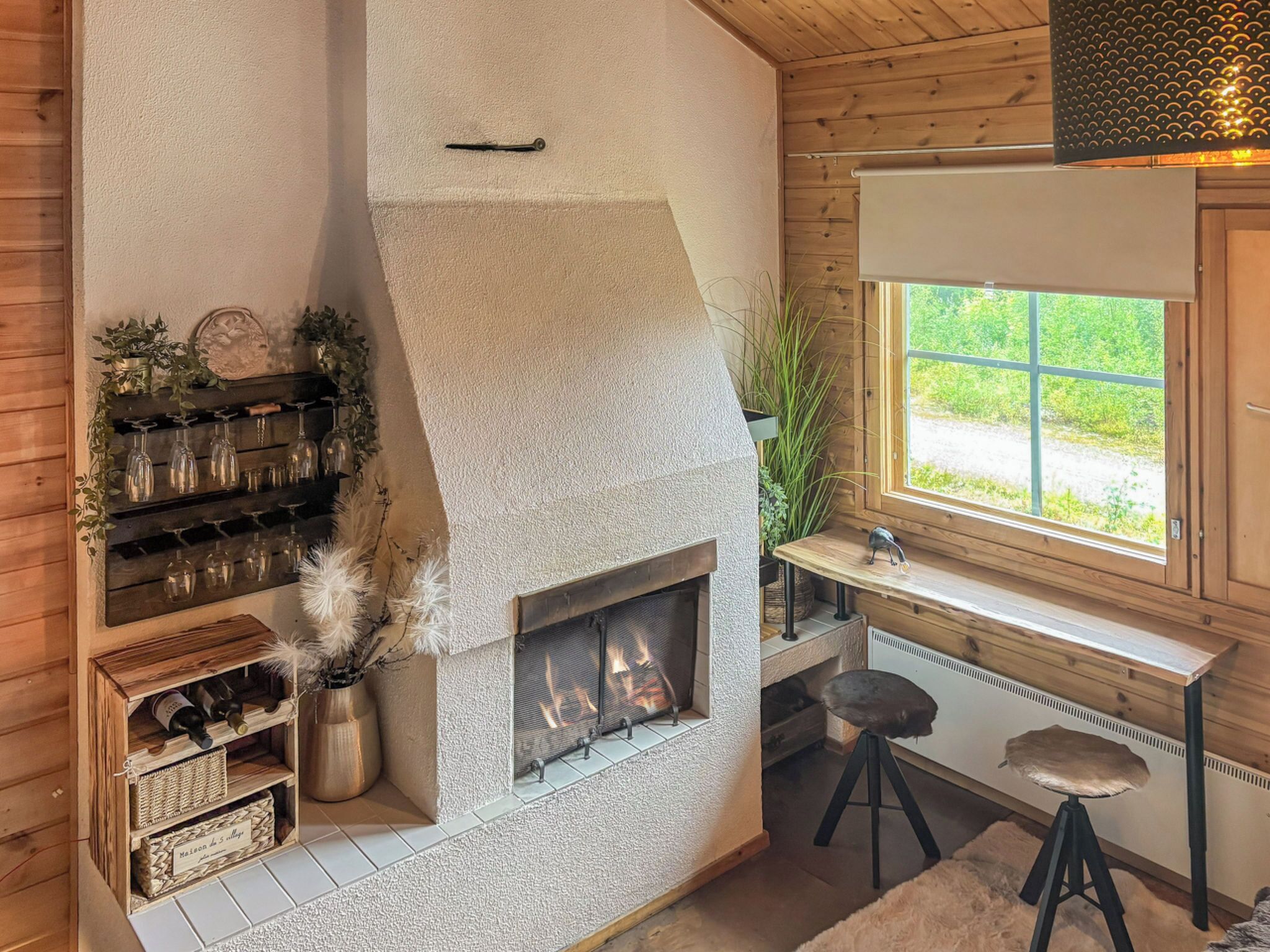 A cozy room with a stone fireplace, wooden shelves with wine glasses, a window with a view, and a small stool.