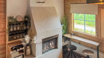 A cozy room with a stone fireplace, wooden shelves with wine glasses, a window with a view, and a small stool.