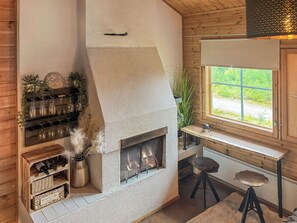 Una habitación acogedora con chimenea de piedra, estanterías de madera con copas de vino, un ventanal con vistas y un taburete pequeño.