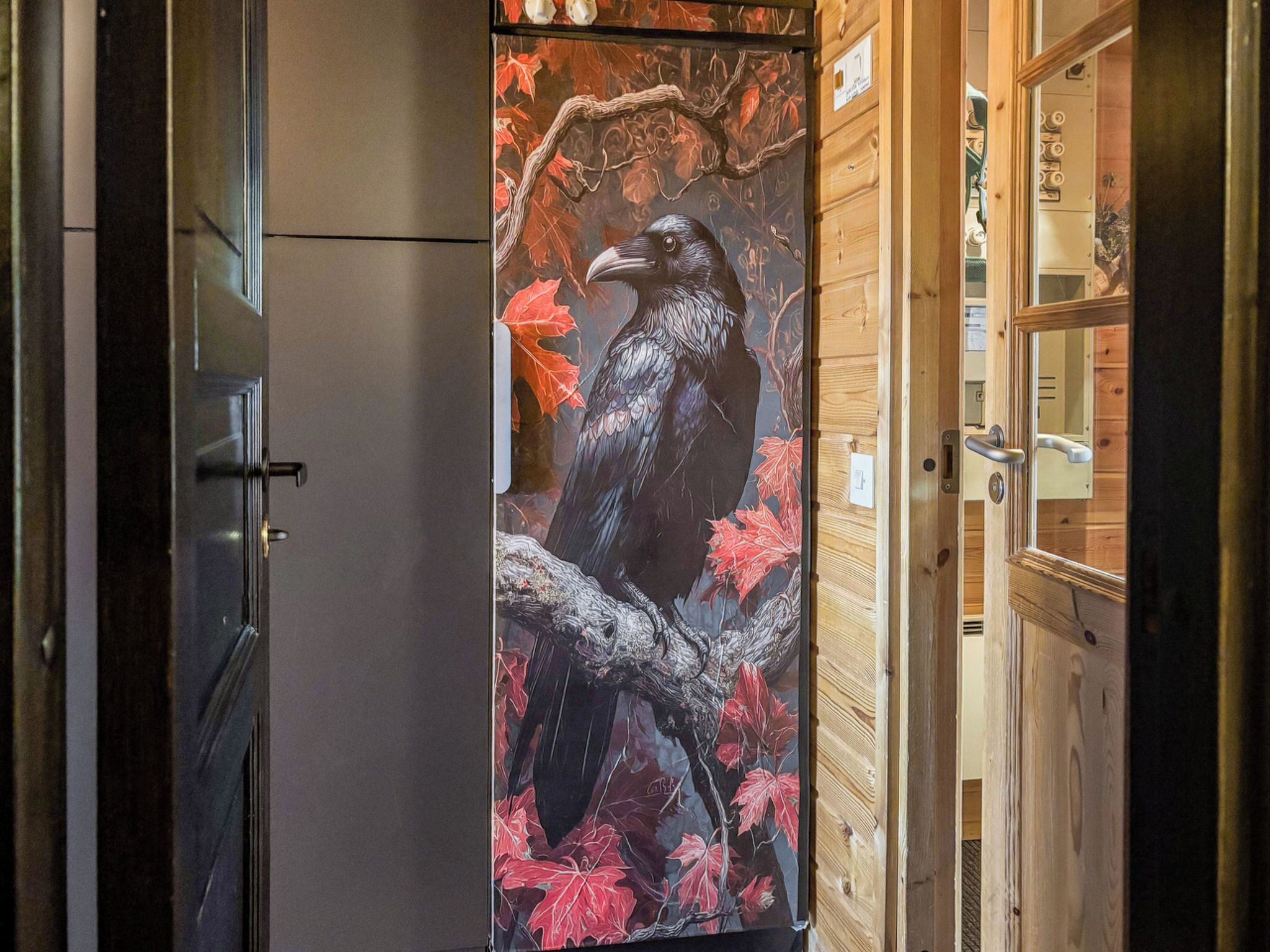 A room with a large painting of a crow on a branch, wooden walls, and a door with a handle.