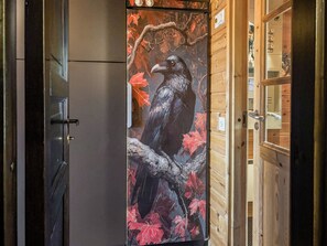 Una habitación con un cuadro grande de un cuervo sobre una rama, paredes de madera y una puerta con picaporte.