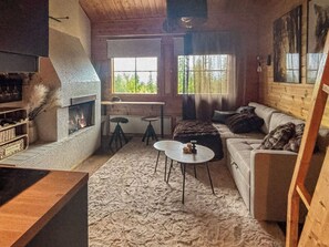 Un interior de cabaña acogedor con chimenea, un sofá, una mesa y una estantería.
