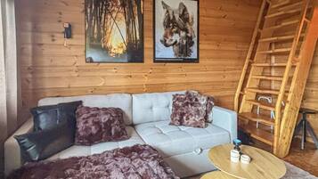 A cozy cabin interior with a sofa, two framed pictures, a wooden ladder, and a round wooden table.