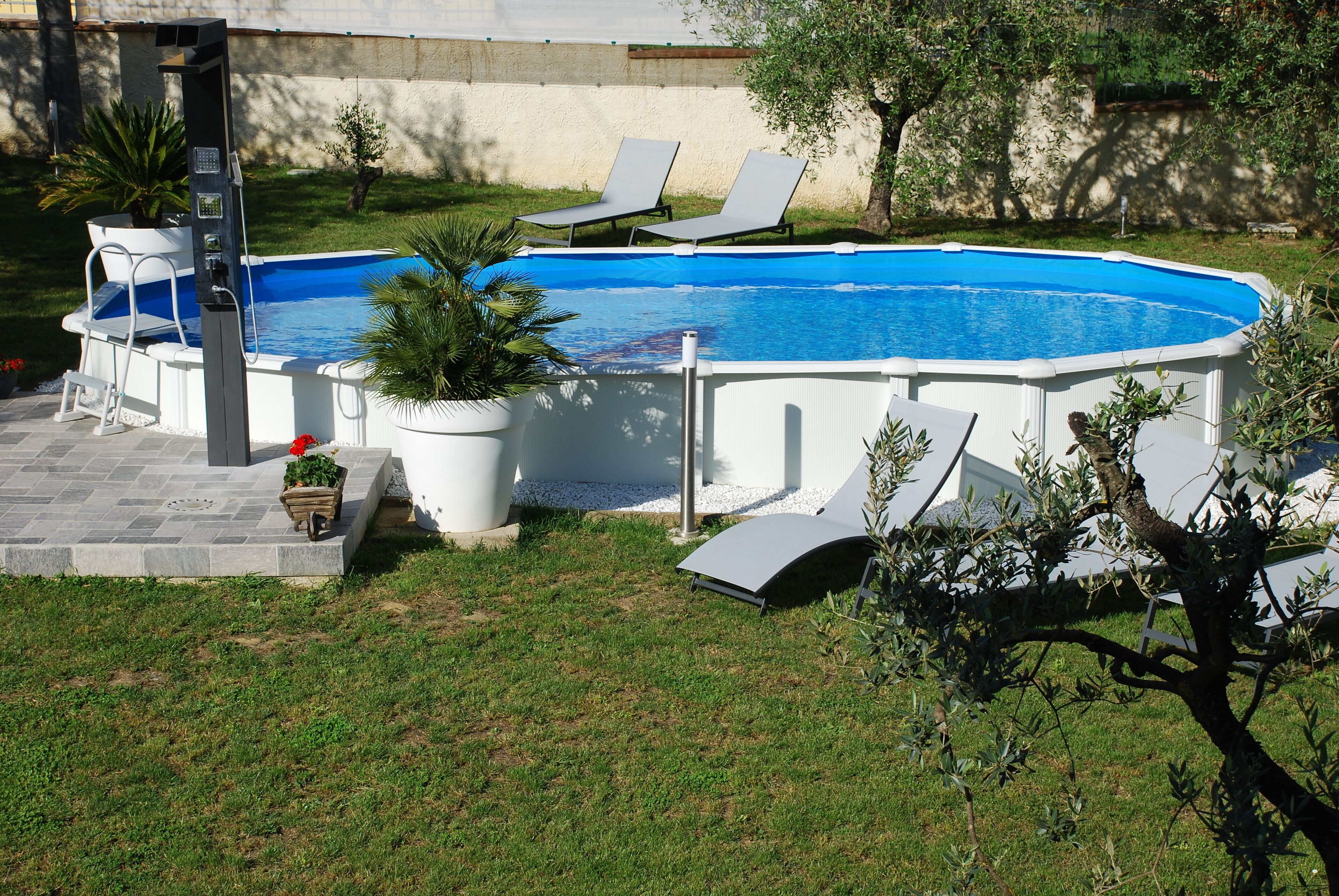 Une piscine hors sol, agrémentée de deux chaises longues et d’une petite terrasse avec une chaise et des plantes en pot.