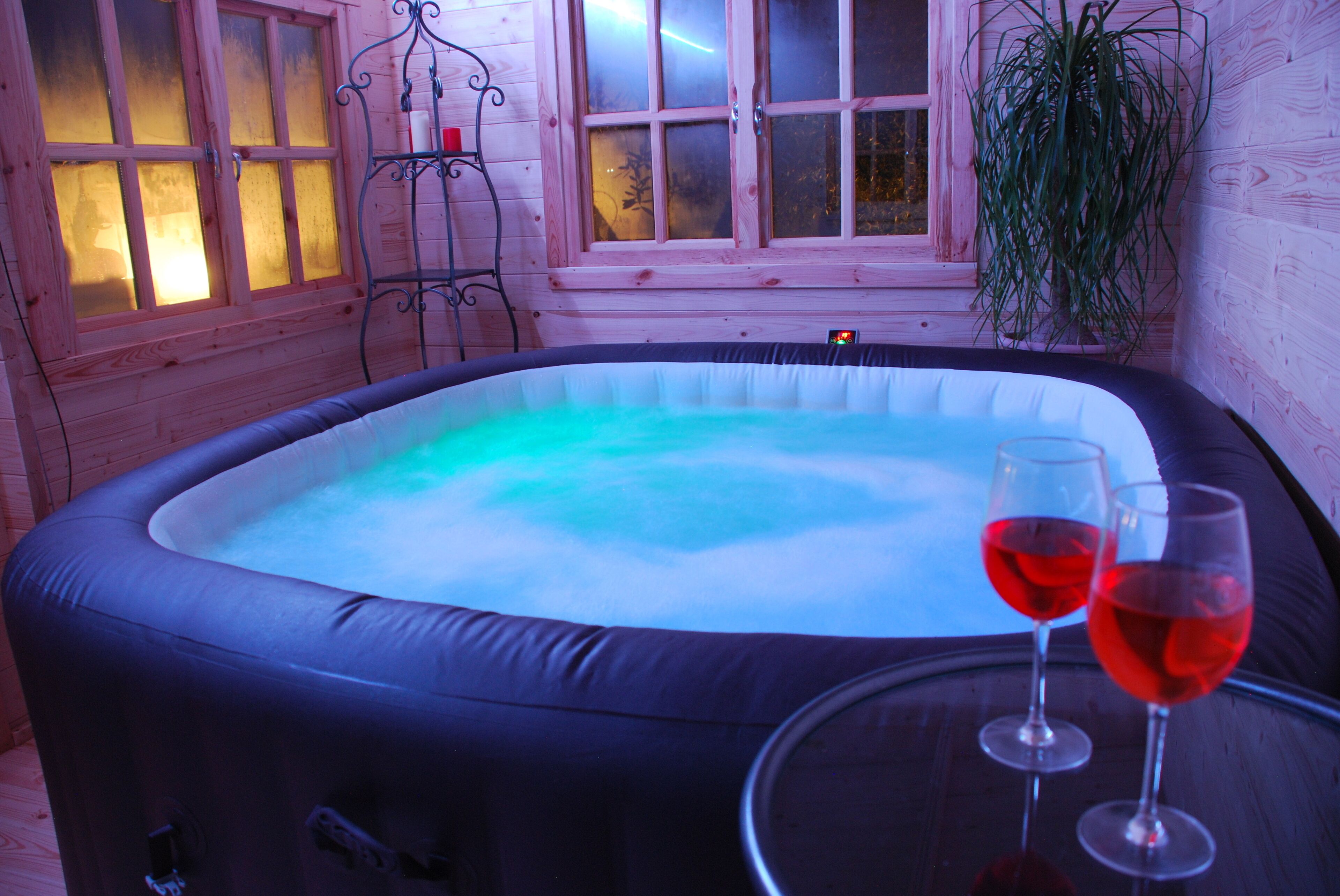 An indoor hot tub with two glasses of red wine on a table.