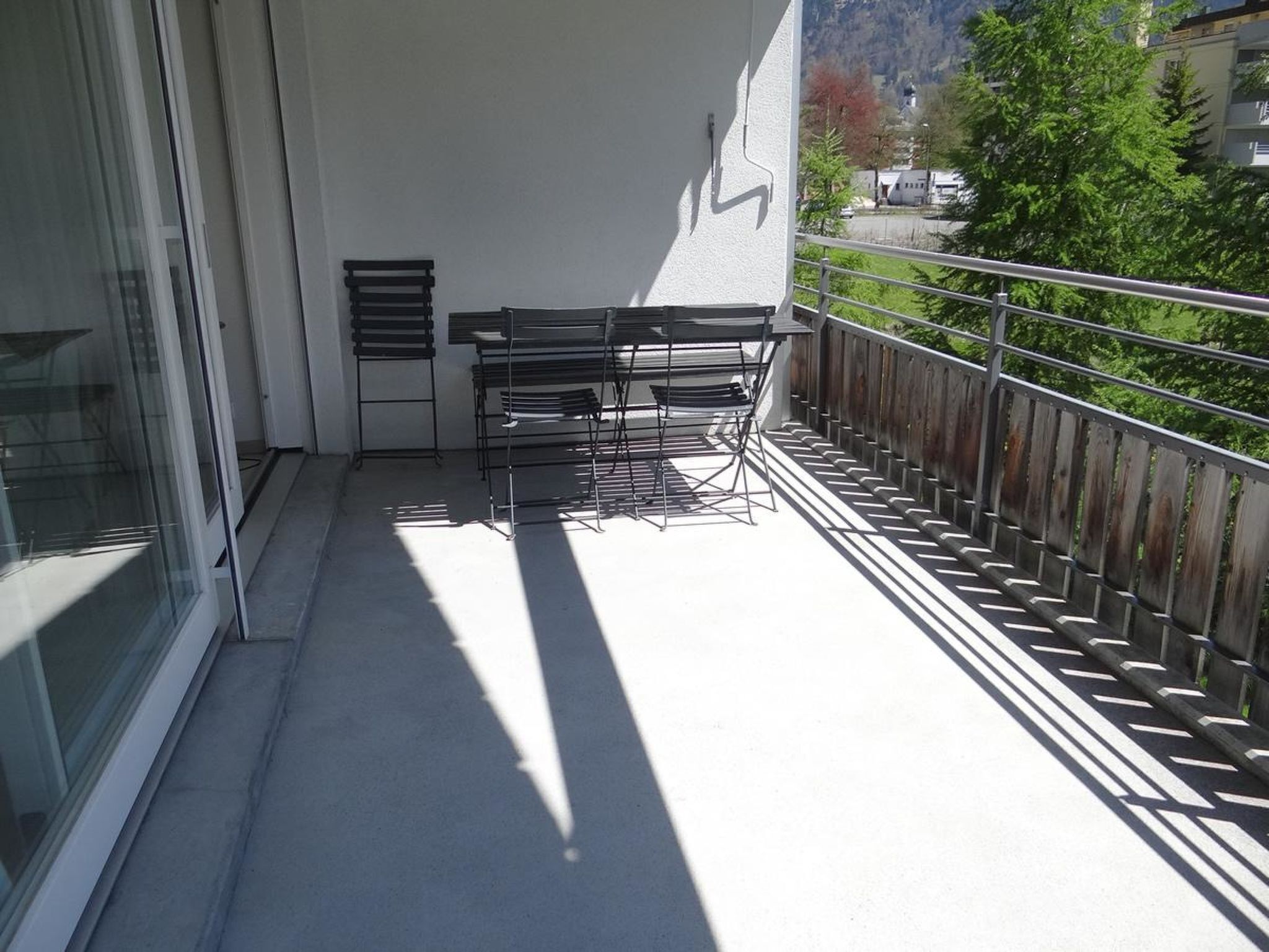 Varanda com mesa e cadeiras, porta de vidro e vista para uma montanha e árvores.