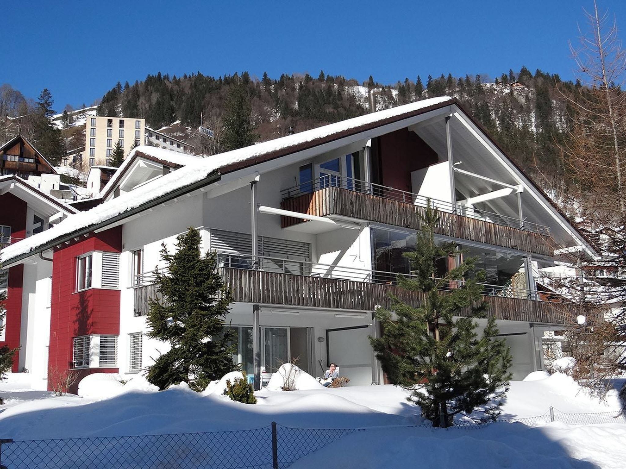 Een chalet met twee verdiepingen en een balkon, omgeven door met sneeuw bedekte bomen en een bergachtig landschap.