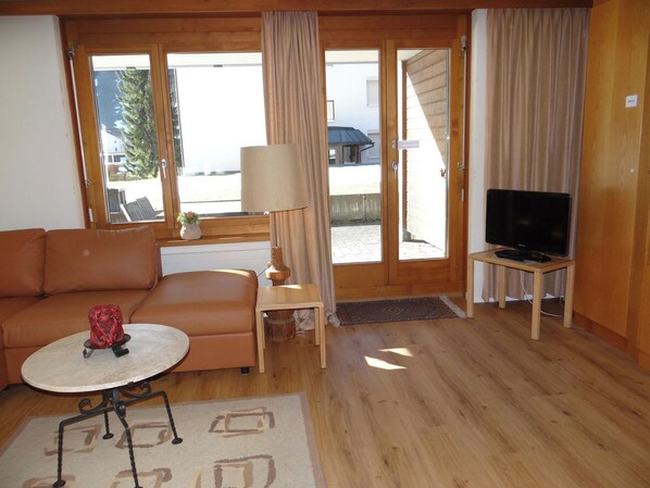 A cozy living room with a sofa, a small table, a lamp, and a TV on a stand.