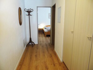 A hallway with wooden flooring, a coat rack, a bed in the background, and a wardrobe.