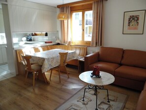 A modern kitchen with white cabinets, a dining table with chairs, a brown leather sofa, and a small round table with a decorative item.