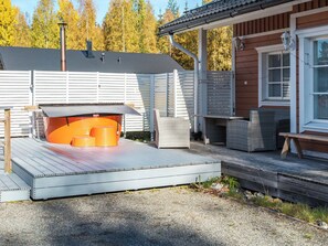 A covered outdoor seating area with a grill, a wooden deck, and a building with a window and a door. - Alppituulahdus by Interhome (Nilsiä)