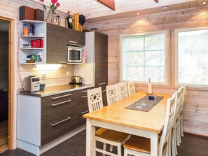 A compact kitchen with modern appliances, a dining area with a wooden table and chairs, and a large window providing natural light.