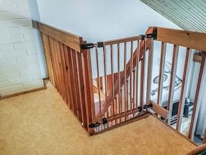 Un escalier en bois avec une rampe en métal, menant à une pièce dont un mur est en briques blanches et qui possède une fenêtre.