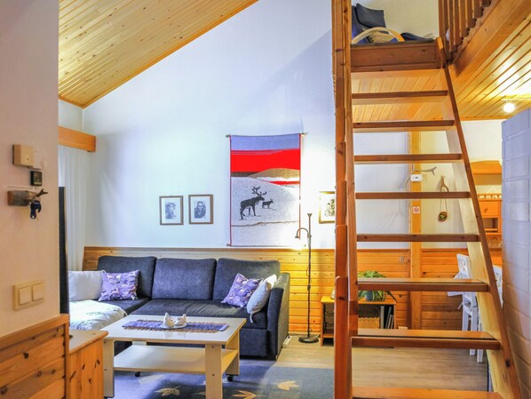 A cozy room with a wooden ceiling, a sofa, a table, and a ladder leading to a loft area.