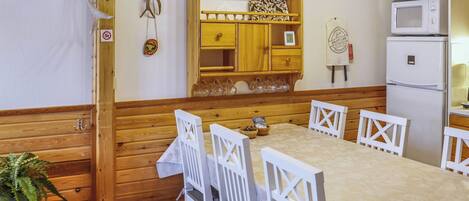 Un interior de madera con una mesa de comedor, sillas blancas, un armario de madera, un microondas y una planta pequeña.