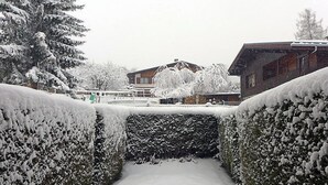 Un sendero cubierto de nieve flanqueado por setos que conduce a un edificio con techo inclinado.