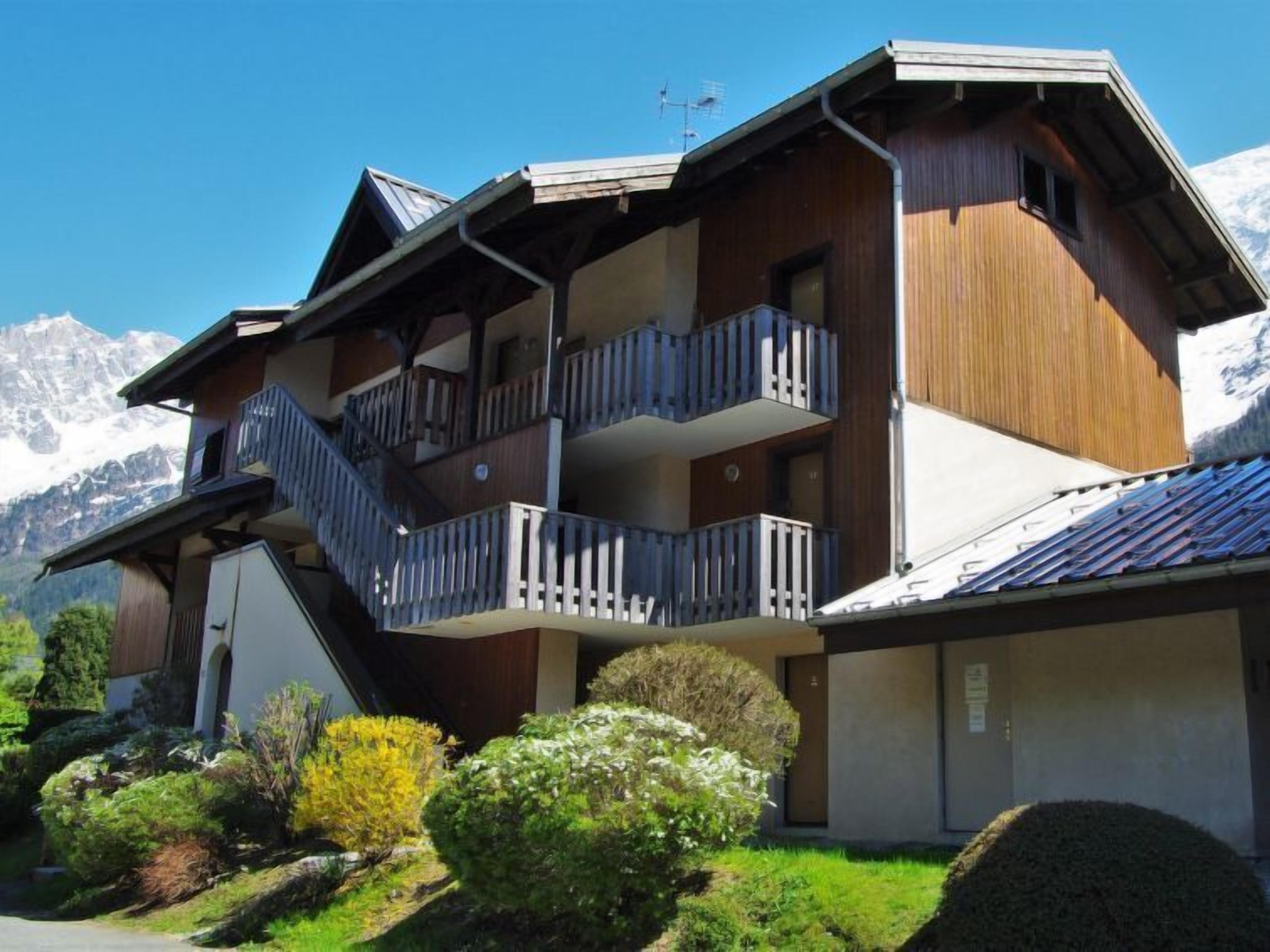A multi-story chalet with balconies, set against a mountainous backdrop.