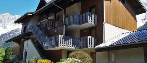 A multi-story chalet with balconies, set against a mountainous backdrop.