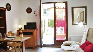 Una habitación acogedora con un escritorio de madera, televisor, cama con ropa de cama roja y puerta corredera de vidrio que da a un espacio exterior.