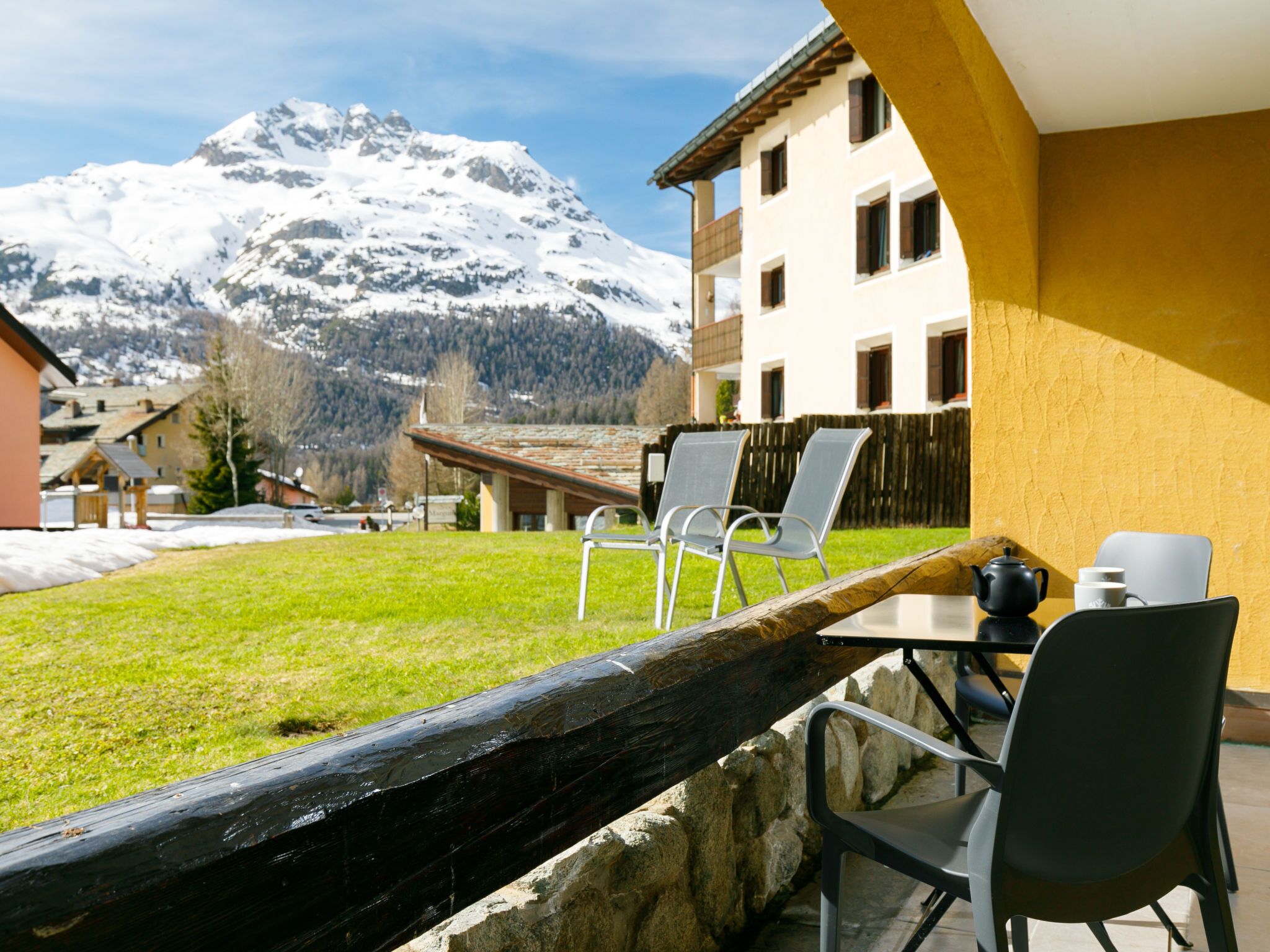 Eine Terrasse mit Außenmöbeln, Blick auf die Berge und ein Gebäude mit gelber Fassade.