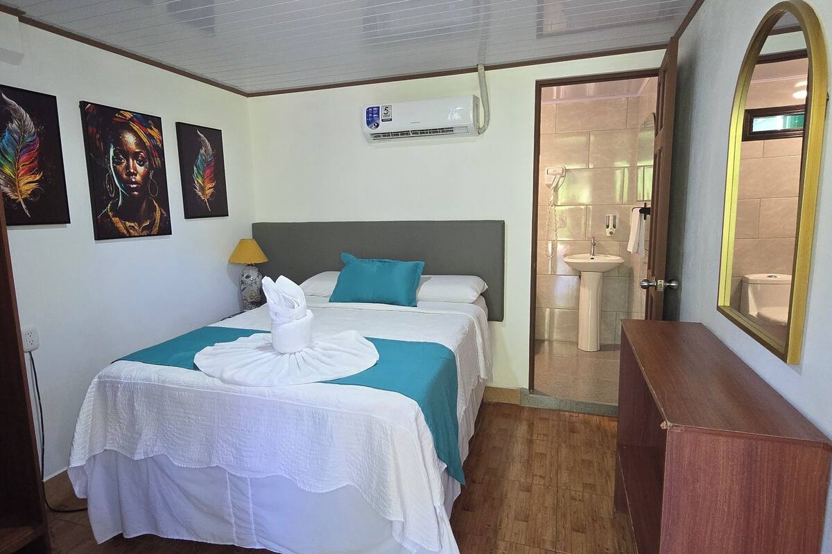A hotel room with a bed, a desk, a mirror, and a bathroom visible through an open door.